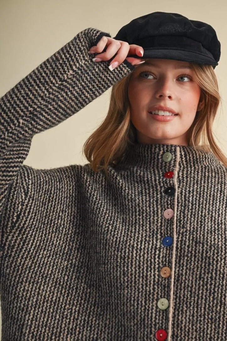 Model wearing a Trestles Clothing Company cozy knit sweater with unique mismatched colorful buttons and a black cap