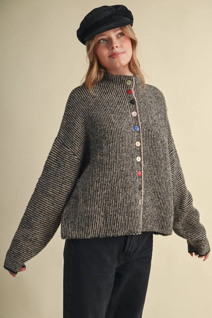 Model wearing a Trestles Clothing Company cozy grey knit sweater with unique mismatched buttons and a black cap