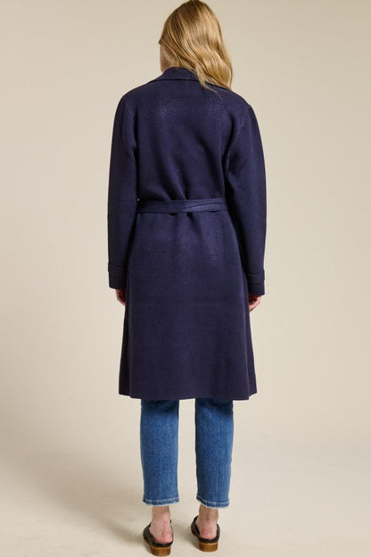 Back view of a woman wearing a navy blue Trestles Clothing Company Beckham midi sweater coat with a belted waist.