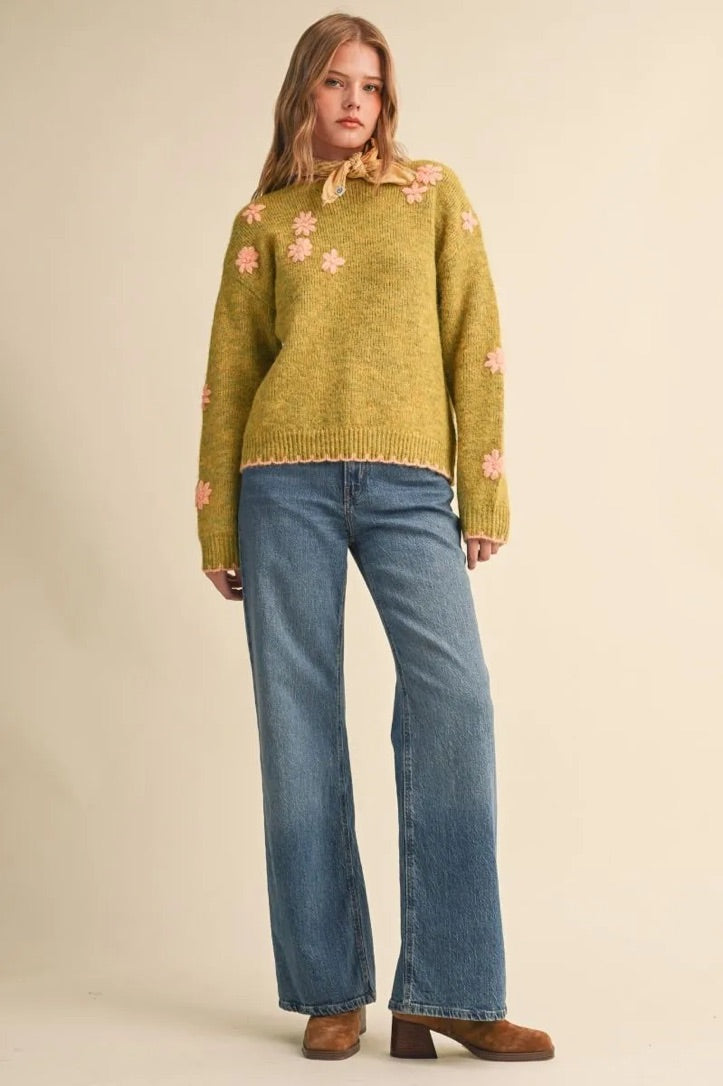 Trestles Clothing Company olive green knit sweater with pink floral embroidery and scalloped edges worn with blue jeans