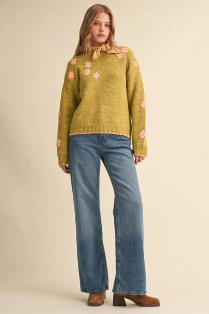 Trestles Clothing Company olive green knit sweater with pink floral embroidery and scalloped edges worn with blue jeans