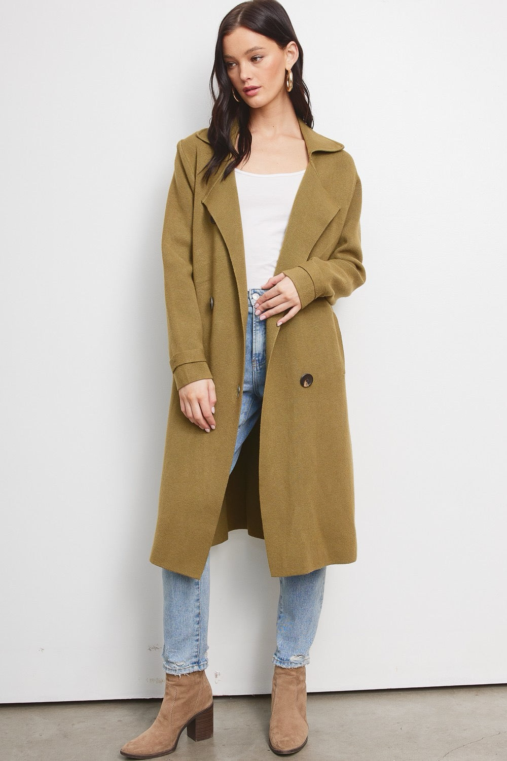 Model wearing a Trestles Clothing Company Beckham midi sweater coat in olive green over a white top and blue jeans.