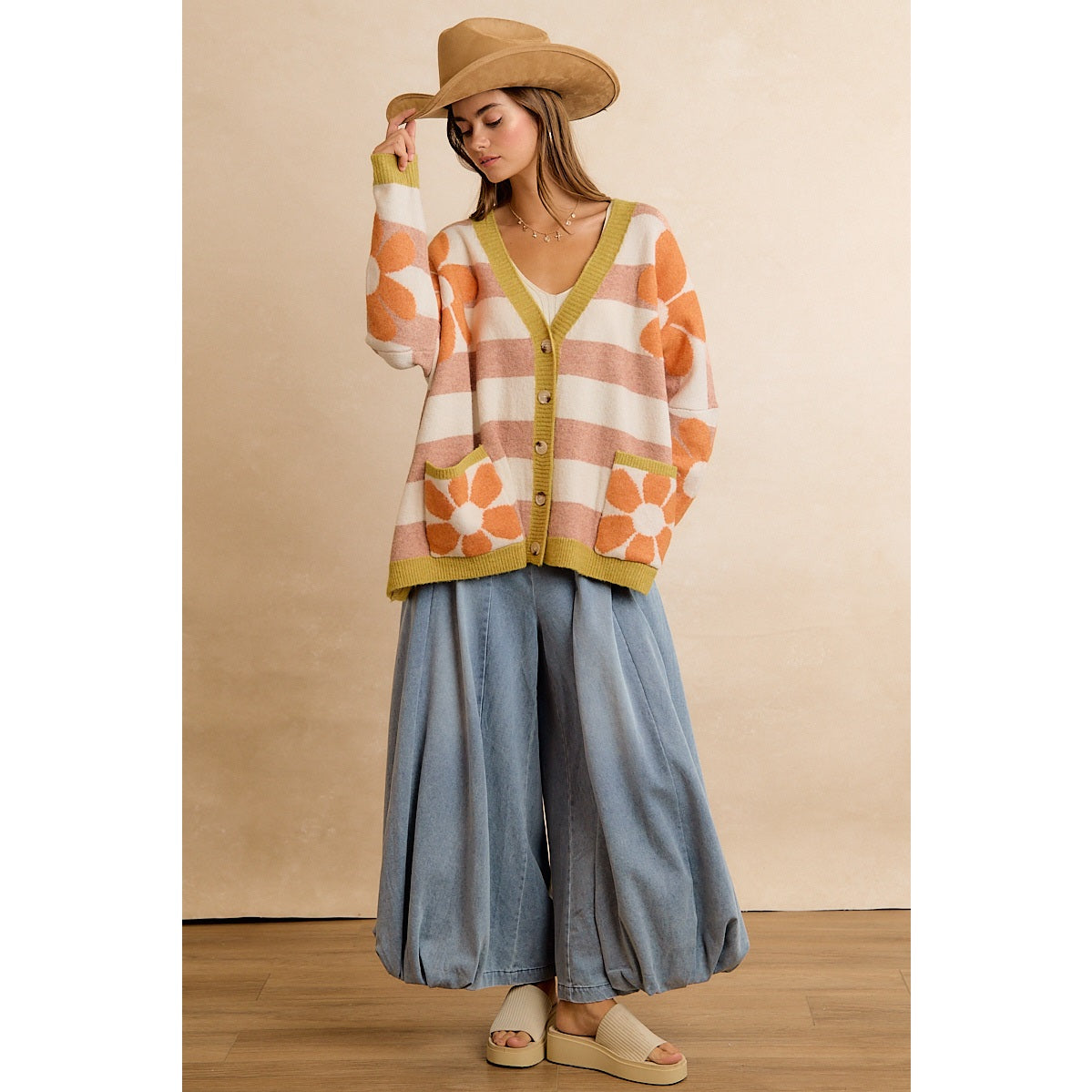 Trestles Clothing Company oversized knit cardigan with orange flowers and stripes, worn with a hat and wide-leg jeans.
