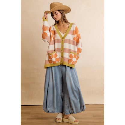 Trestles Clothing Company oversized knit cardigan with orange flowers and stripes, worn with a hat and wide-leg jeans.