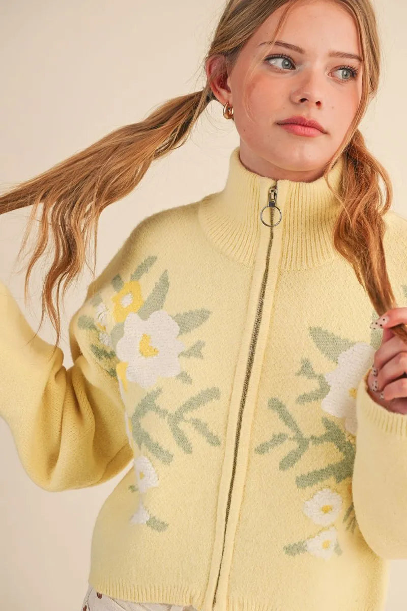 Trestles Clothing Company yellow floral knit zip-up sweater with a stand collar and puff sleeves on a young woman