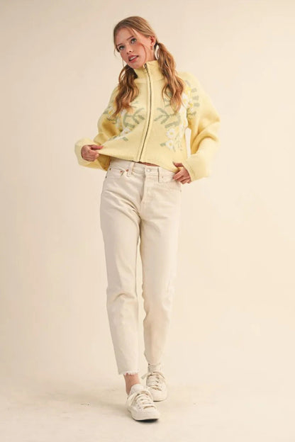 Trestles Clothing Company yellow floral knit zip-up sweater with puff sleeves worn with white jeans by a blonde model